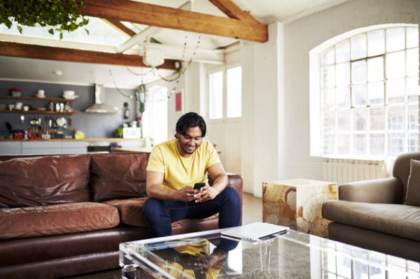 A guy uses his mobile phone whilst sitting on sofa