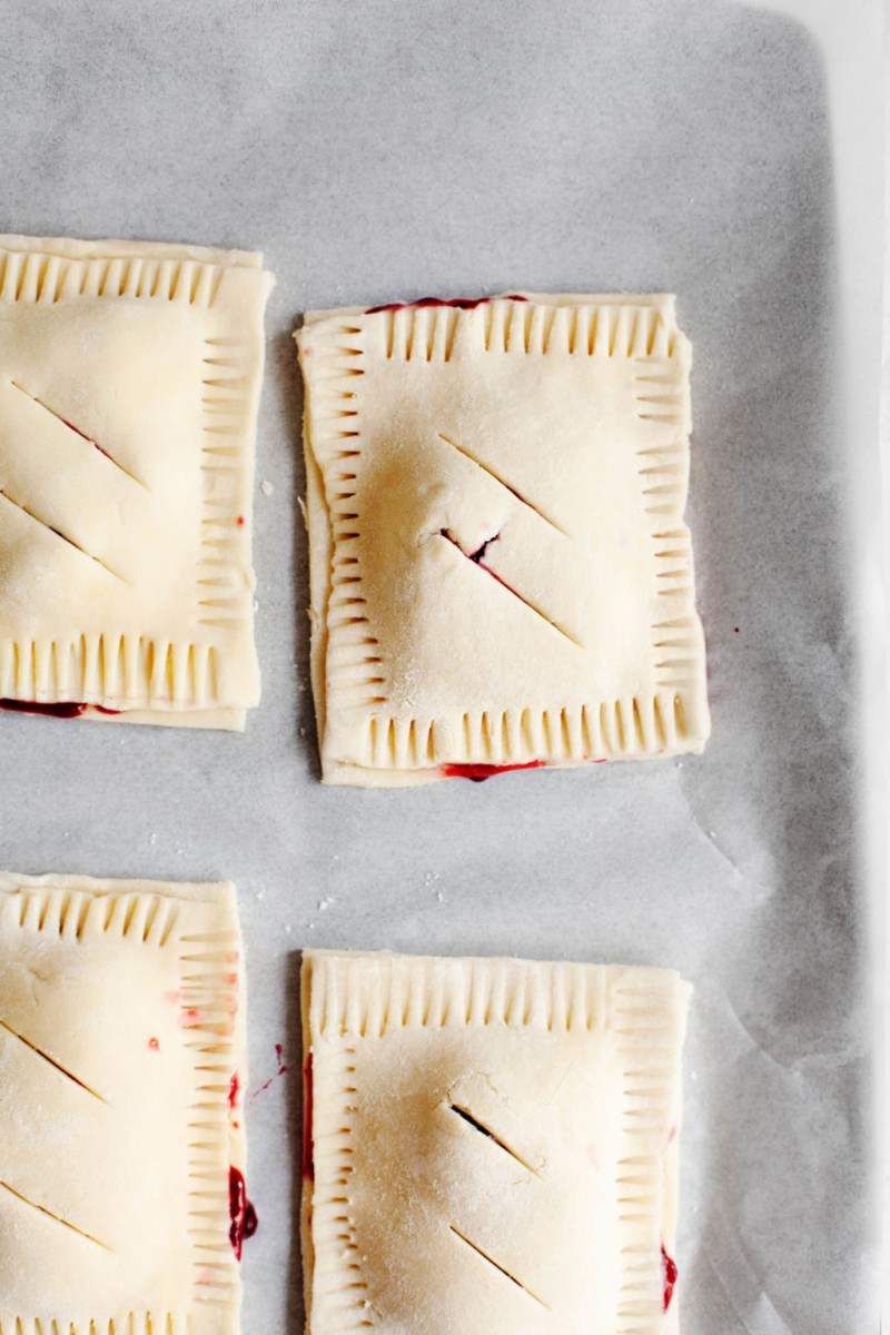 The pastry for hand pies has been assembled onto a baking sheet and stuffed with a cherry filling. The hand pies have been crimped and vented before baking in the oven.