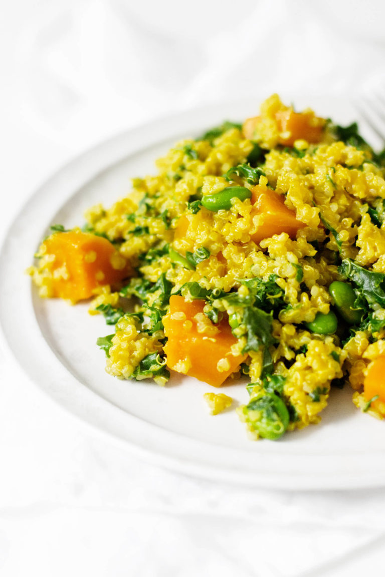 An angled photograph of a protein rich vegan meal, made with quinoa, edamame, squash, and greens.