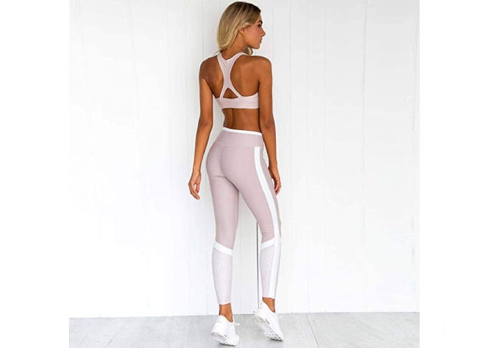 A back view of a woman wearing matching set of light pink and white sports bra and leggings.