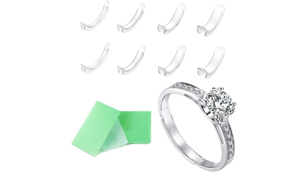 Eight clear ring adjusters above a silver diamond ring with a green cleaning cloth.