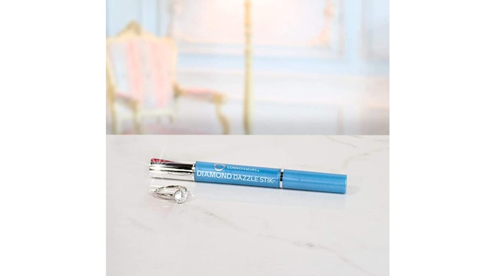 A blue and silver jewelry cleaning pen sitting on a white marble counter next to a diamond ring.