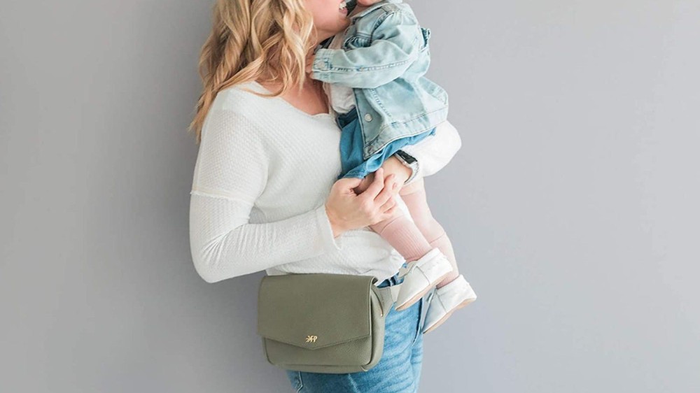 mom holding toddler and wearing a green Freshly Picked fanny pack