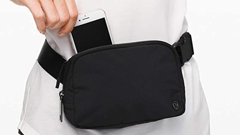 black fanny pack on woman's waist while she pulls her iPhone out