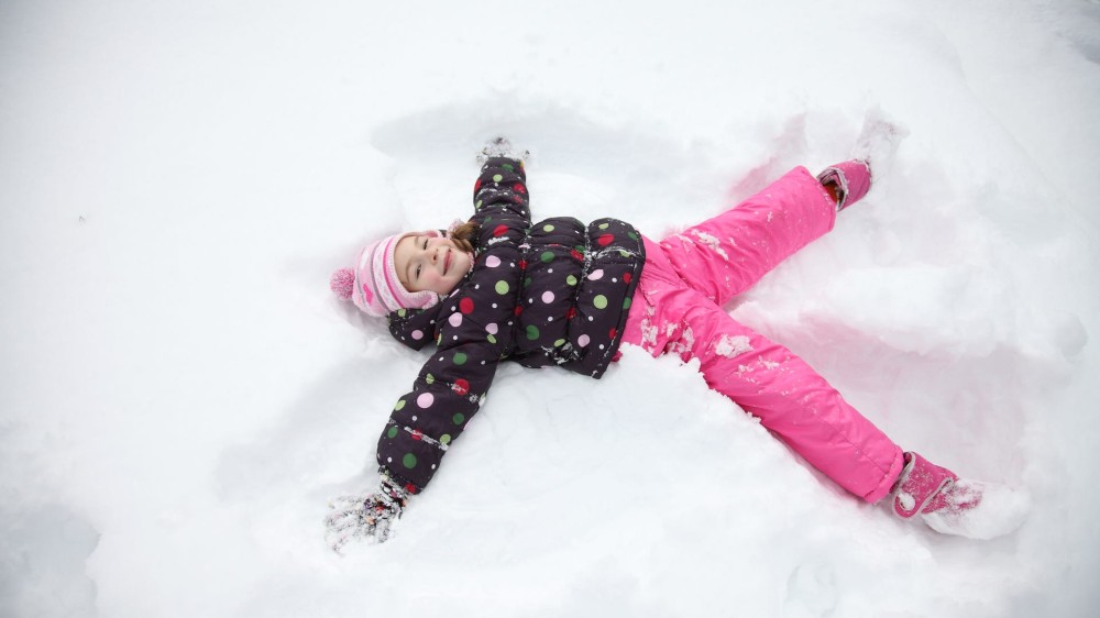 A girl makes a snow angel in the snow in her snow gear.