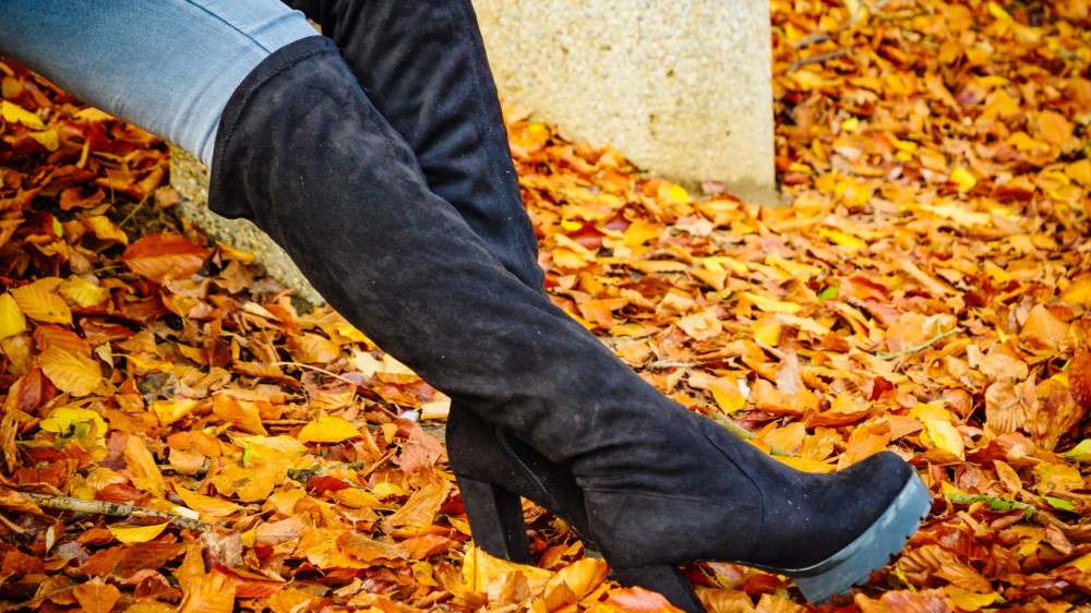 A woman wears long black heeled knee high boots and jeans.