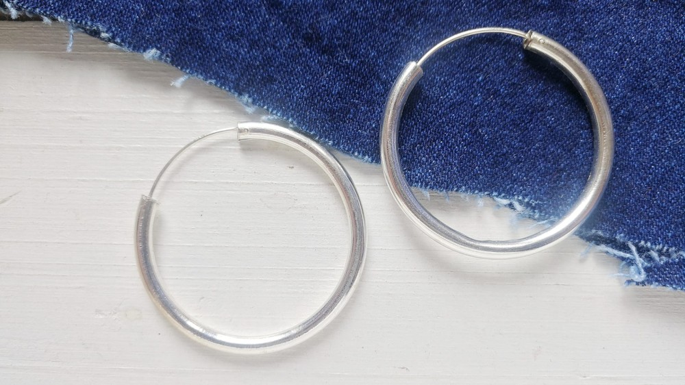 two silver hoop earrings on a white and denim surface.