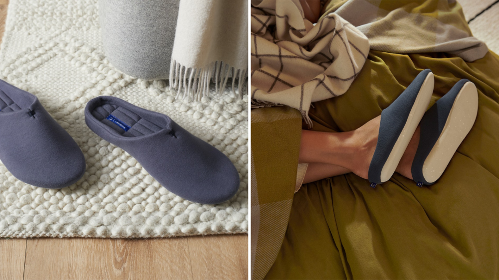 A pair of slippers sits on a rug, and a person wears a pair under a blanket.