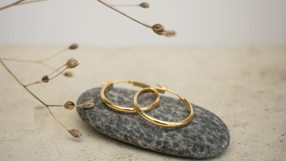 Gold hoop earrings on a stone with a branch in the background.