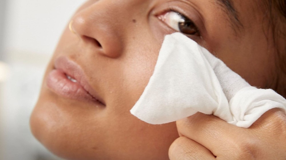 A woman using a makeup remover wipe under her eye.