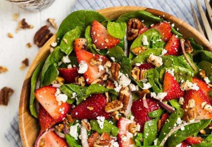 A spinach strawberry salad in a wooden bowl.