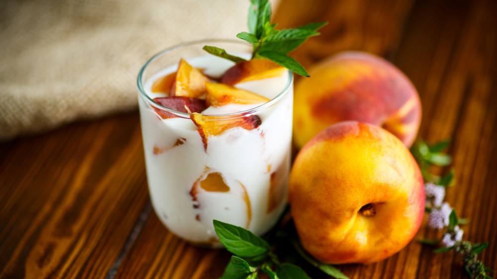 Yogurt and sliced peaches in a glass cup with two peaches next to it. 