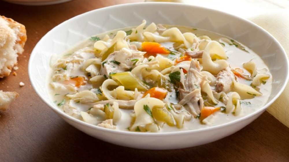 A bowl of hot chicken noodle soup filled with celery, carrots, egg noodles and parsley.