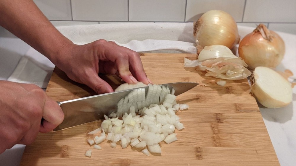 Dicing an onion in uniform peices with peels and onions in the background. 