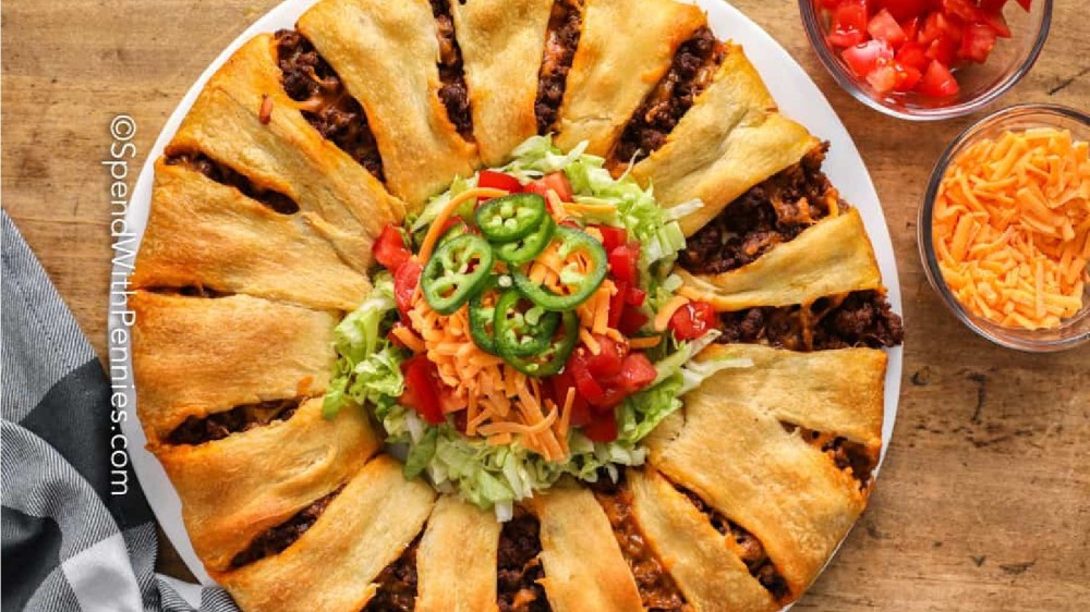 A taco crescent ring filled with meat and cheese with lettuce tomato and shredded cheese in the middle.