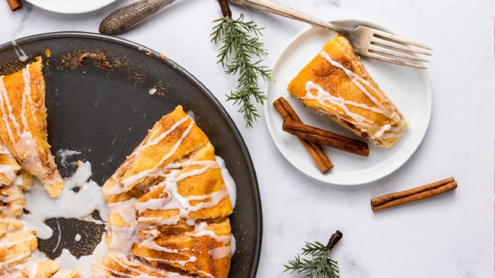 Cinnamon and cheesecake wreath on a round pan next to a plate with a slice of it on it. 