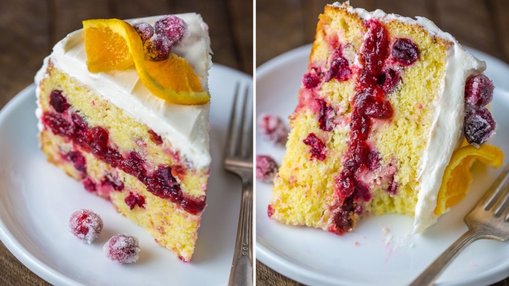 Two slices of orange cake with cranberry filling, white frosting, and an orange slice and berries on top