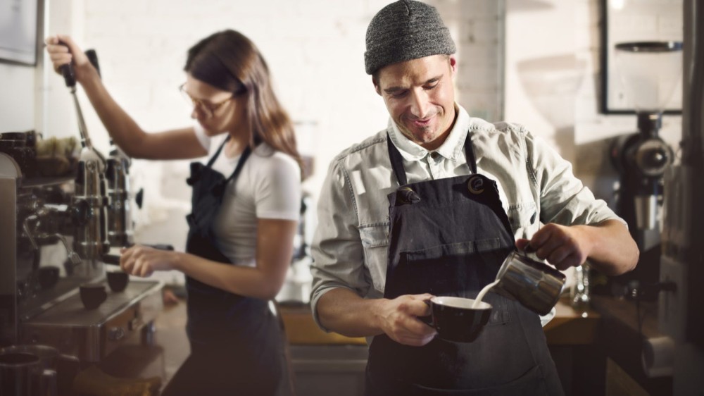 Two baristas working in tandem to create some delicious coffee drinks at a coffee shop.