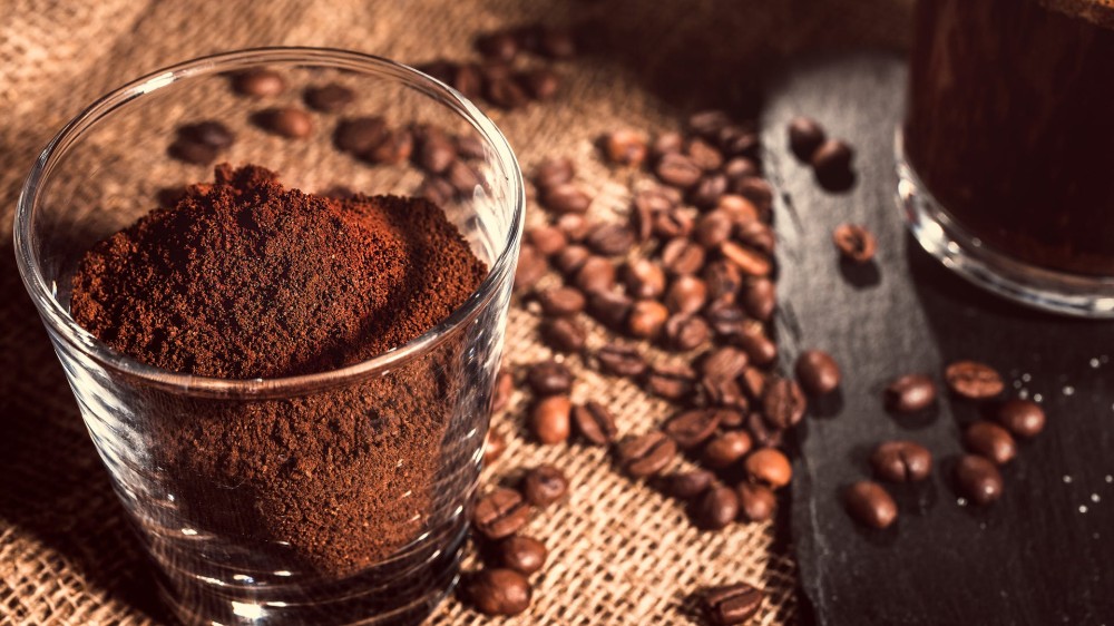 black coffee in a glass cup on a background of burlap next to coffee beans and ground coffee