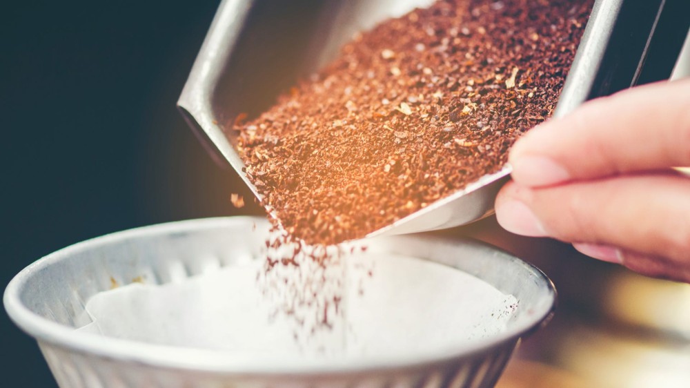 Hands pour coffee grounds into a coffee filter.