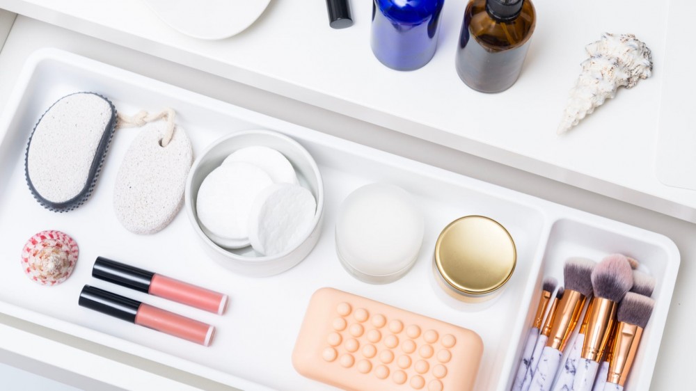 an open drawer with a white organizer tray with makeup products and a bar of soap in it.