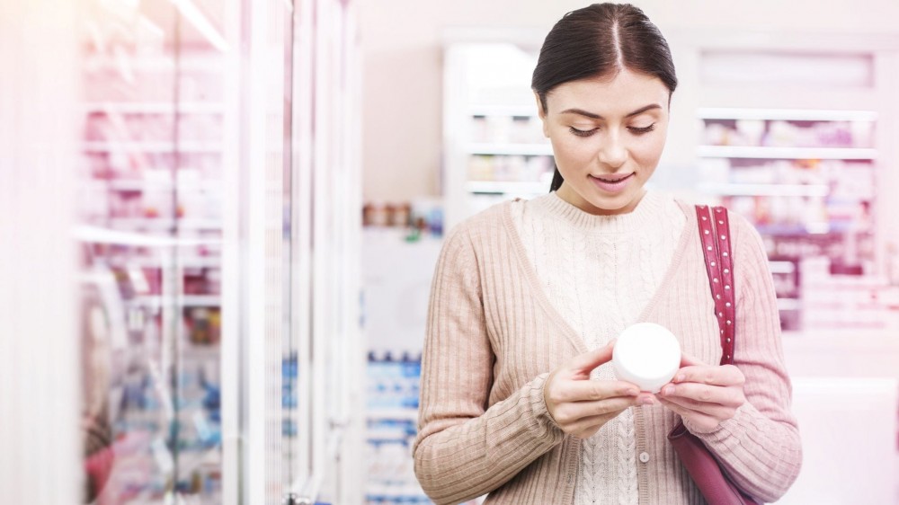 A woman reading a label on the back of a skin care product. 