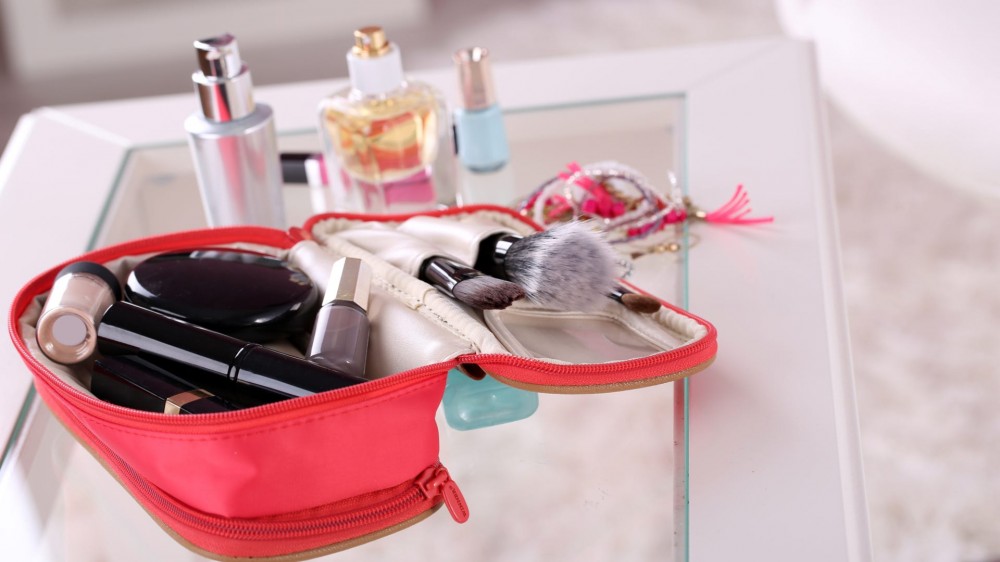 A small and pink cosmetic bag full of makeup products on a table..