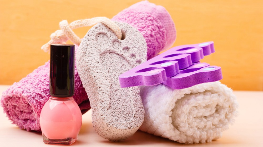 Pedicure accessories: pumice with footprint, towel, toe separators and pink polish.