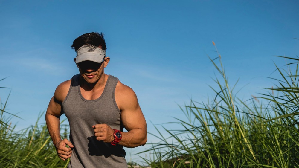 A fit asian man runs through a trail at a grass field during a clear sunny day.