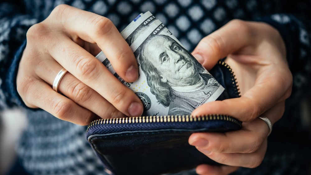 Hands holding U.S. dollar bills and small money pouch.