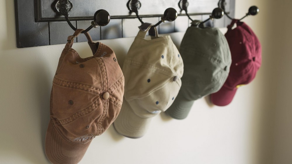 Several caps hang on hooks near a door. Focus on worn cap in foreground.