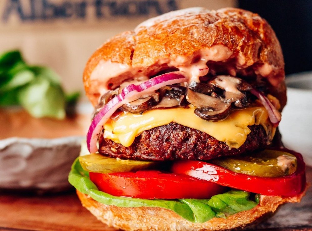 A Beyond Meat Cheeseburger loaded with onions, mushrooms, pickles, lettuce, and tomato. 