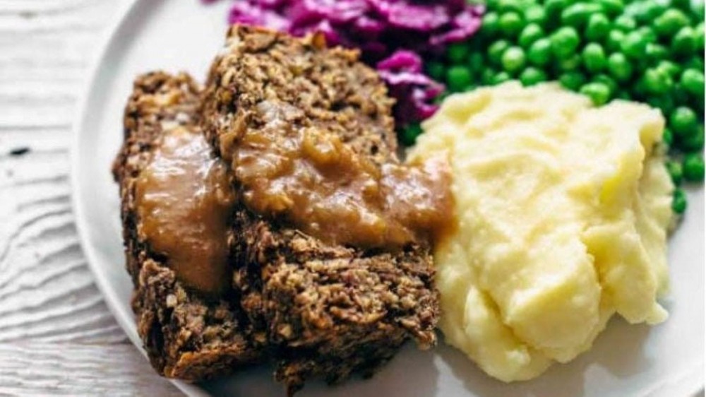 Two slices of veggie meatloaf on a plate with mashed potatoes and peas.