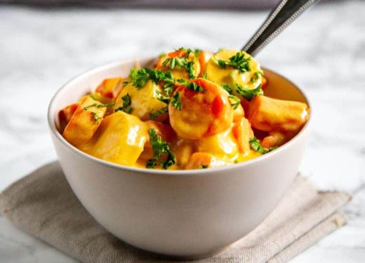 A white bowl of cheesy carrots and parsnips topped with parsley.