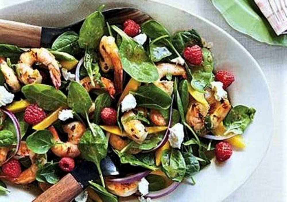 A plate of grilled shrimp and spinach salad. 