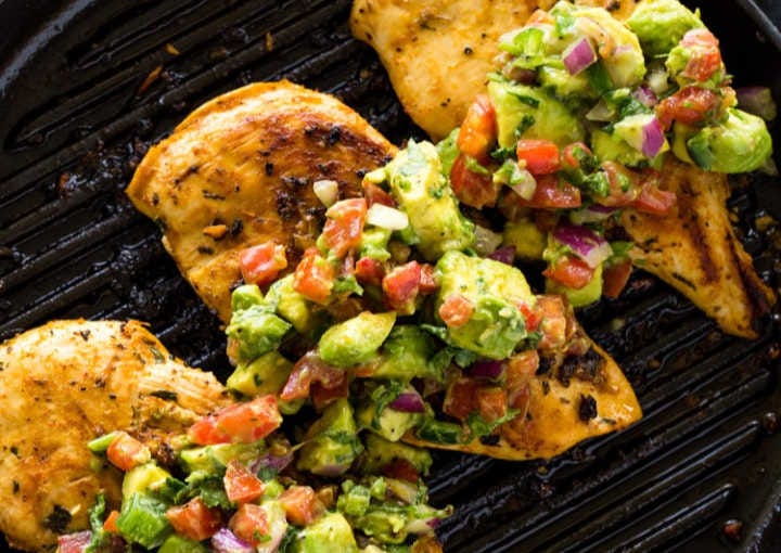 Grilled chicken sizzling in a grill pan, topped with avocado salsa