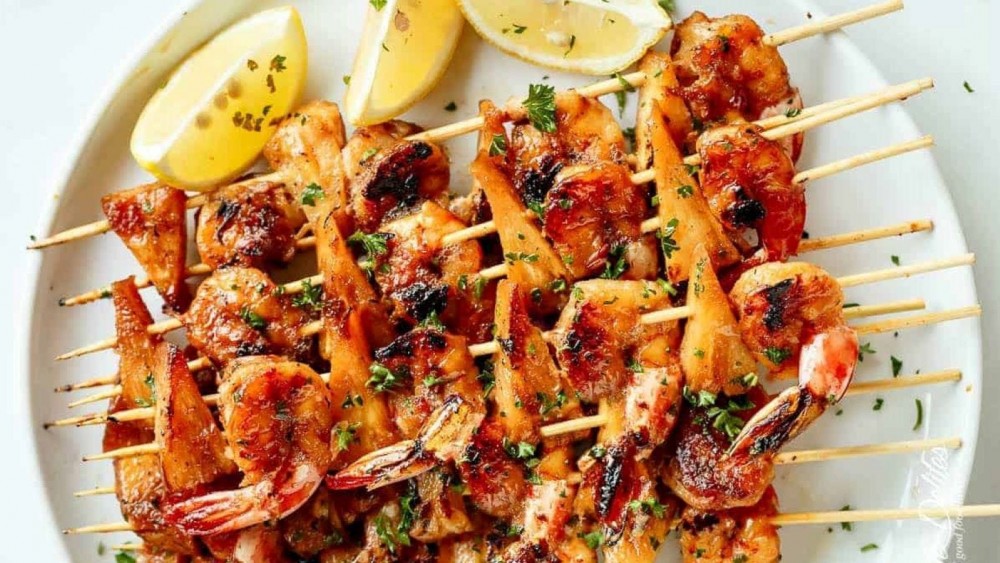 A stack of grilled honey garlic butter shrimp pineapple skewers on a plate with lemon slices. 