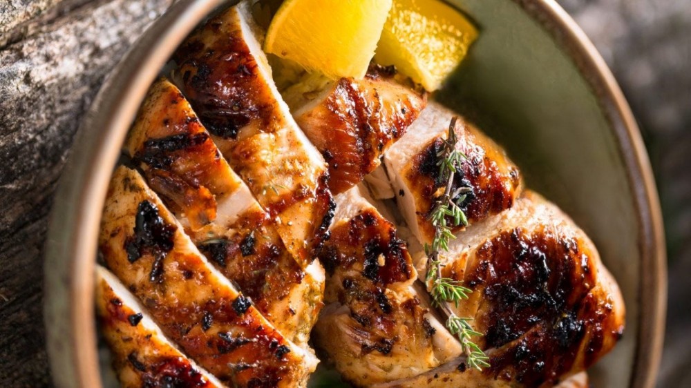 A bowl of sliced grilled chicken with lemon. 