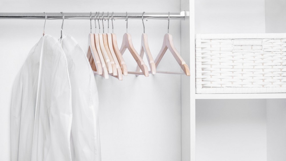 The inside of a white closet with two white garment bags and wooden hangers hanging.