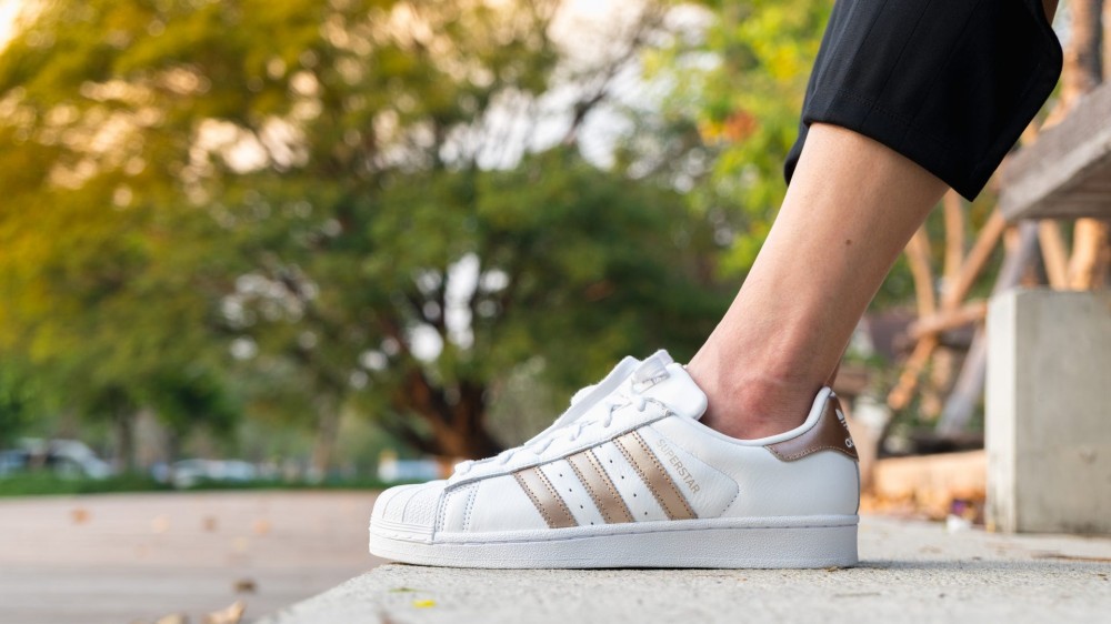 A woman wears white striped adidas shoes outside.