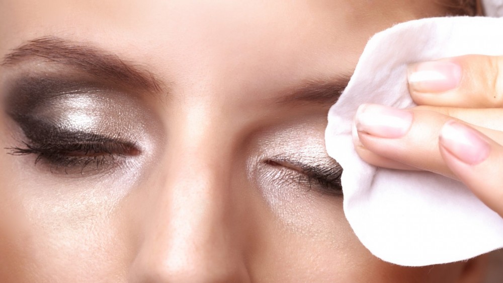 Removing makeup - closeup portrait of a pretty young woman using cotton on closed eyes.