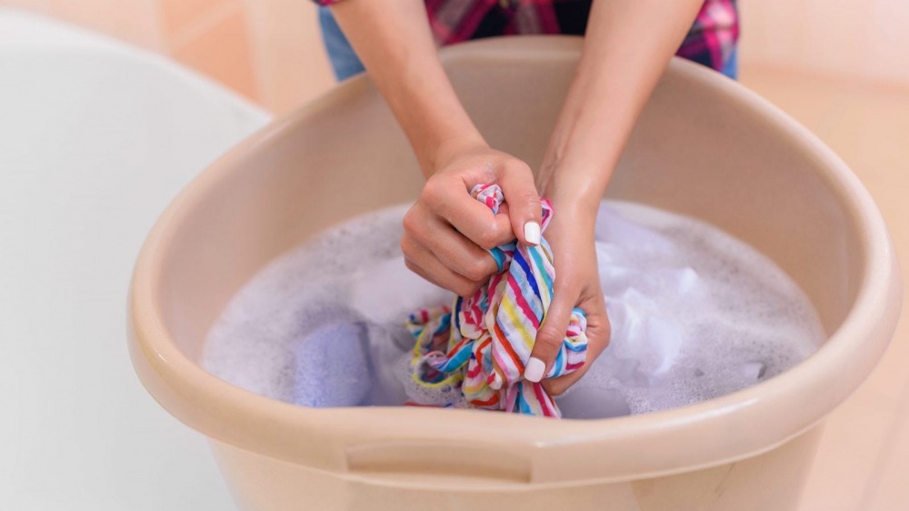 A woman hand washes clothing.