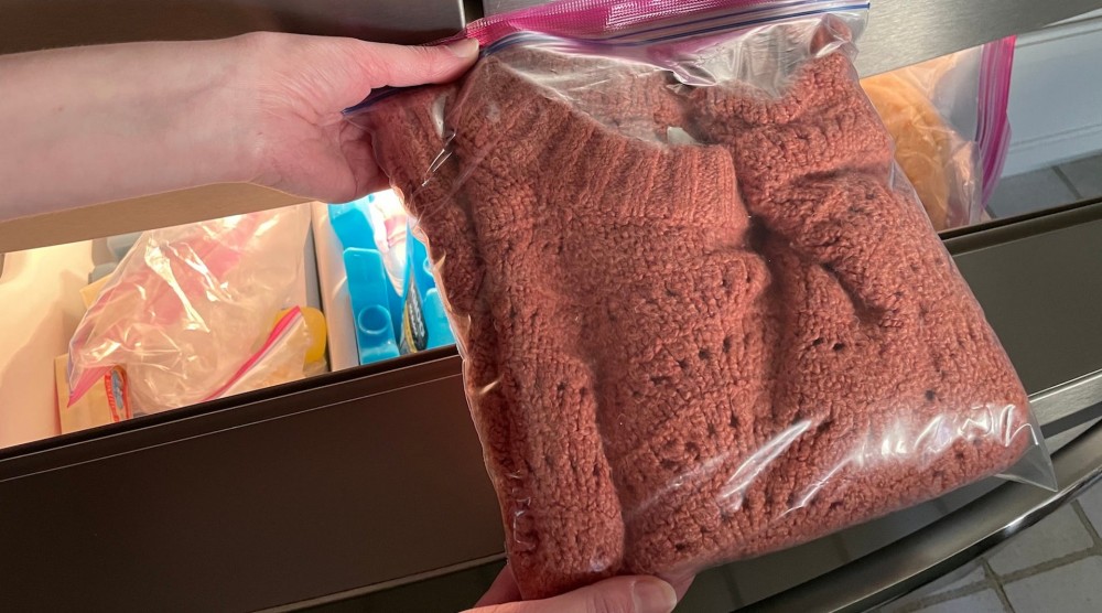 A peach-colored sweater in a plastic bag going into the freezer