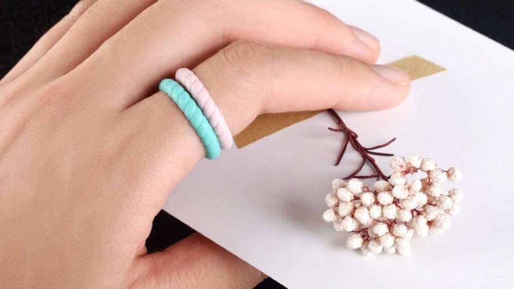 A woman's hand holding a small bunch of flowers and wearing two silicone rings in turquoise and white.