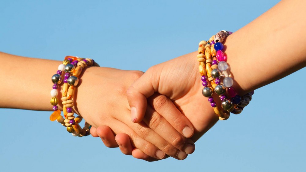 Close-up of two friends holding each other's hands wearing friendship bracelets.