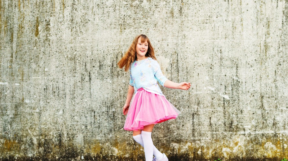 Happy little girl dancing on the street, wearing beautiful tutu skirt and high over knee socks.