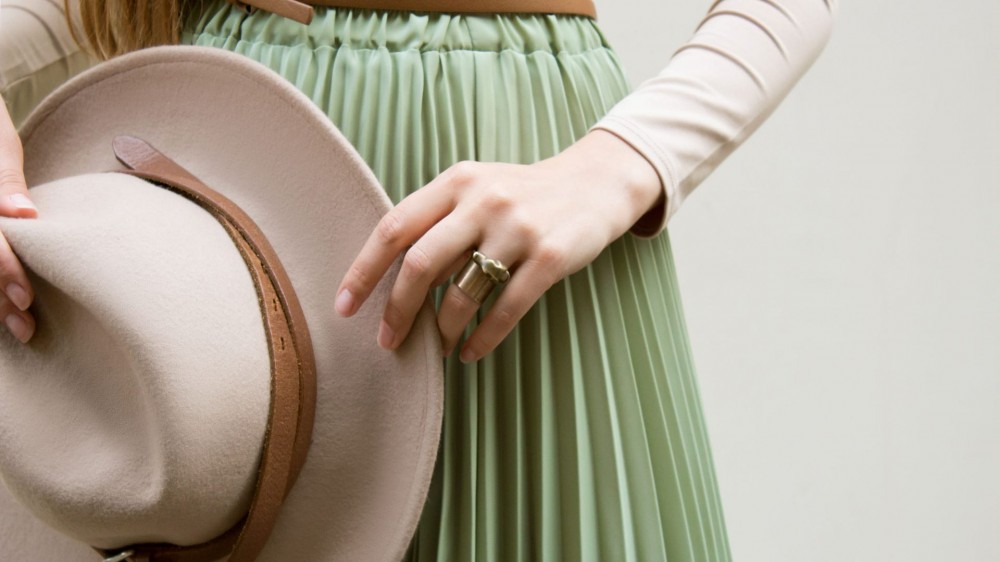 Close-up of a girl holding a beige hat and wearing a light-green pleated skirt.