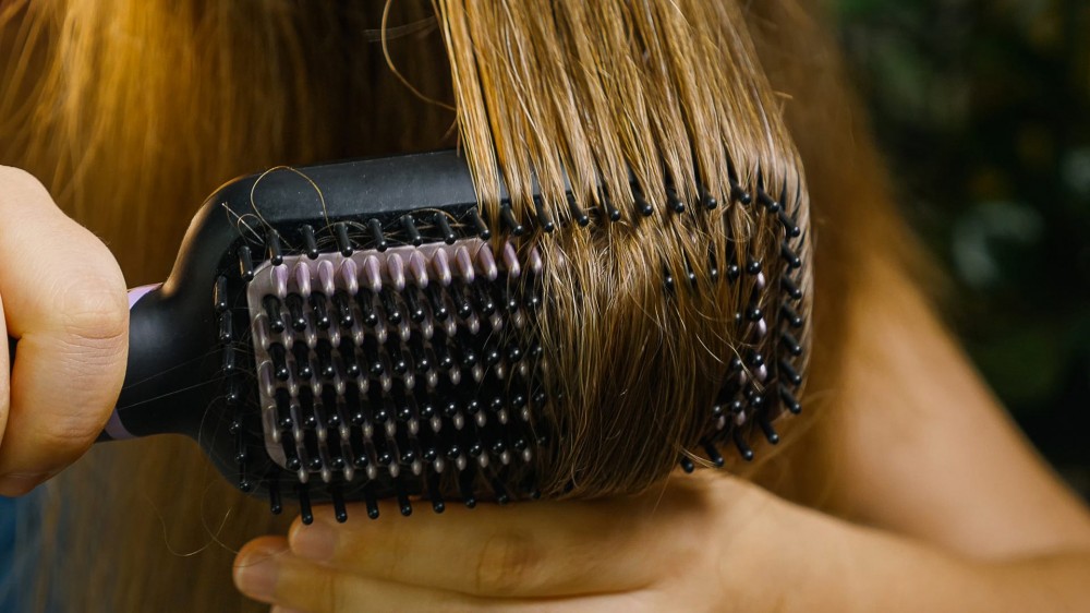 Close-up of a girl brushing and drying her hair with an electric hair straightener.