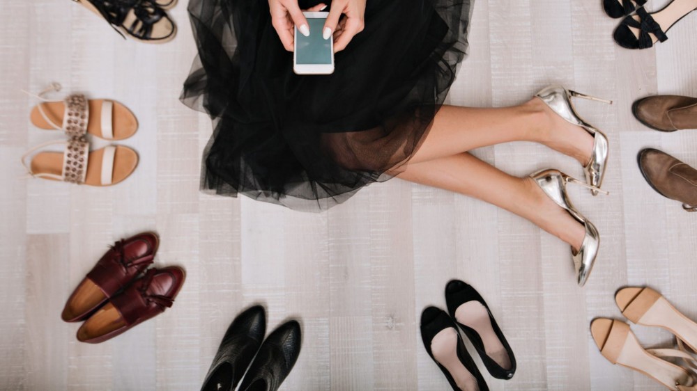 Stylish girl sitting on the floor surrounded by a variety of shoes. 