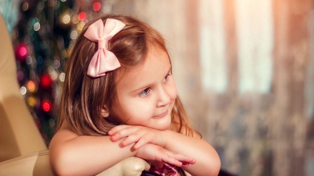 Little girl sitting in chair with a light-pink hair bow.